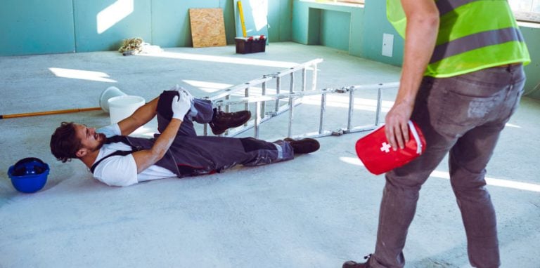 Un homme sur un chantier qui est tombé et quelqu'un arrive avec une trousse de secours